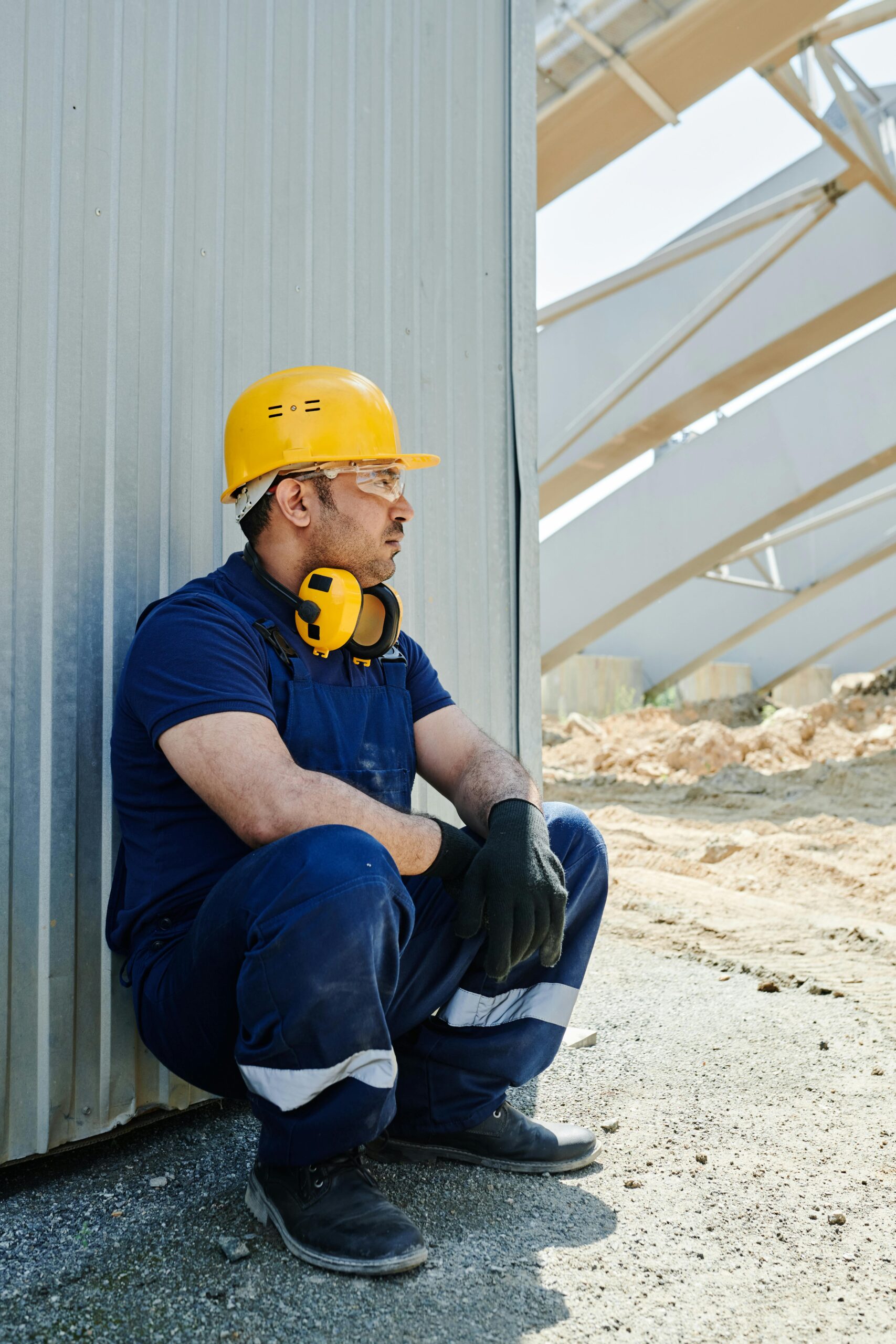 Home Worker in safety gear sits on site taking a break. Outdoor industrial setting.